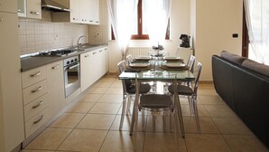 A modern kitchen with a dining area, featuring a glass table, chairs, a sofa, and a stove.