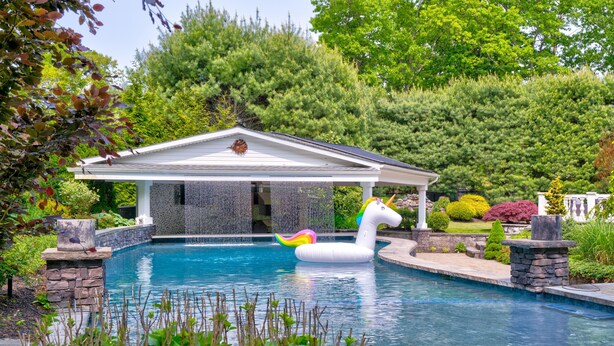 En swimmingpool med en svanebadering, omgivet af stensøjler og frodigt grønt.