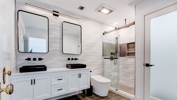 A modern bathroom with a white vanity, two mirrors, a glass shower enclosure, and a white toilet.