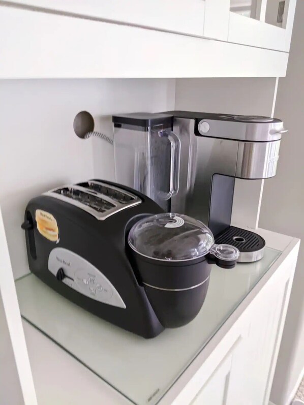 Une cuisine équipée d’un grille-pain, d’une machine à café et d’une bouilloire, le tout posé sur un plan de travail blanc.