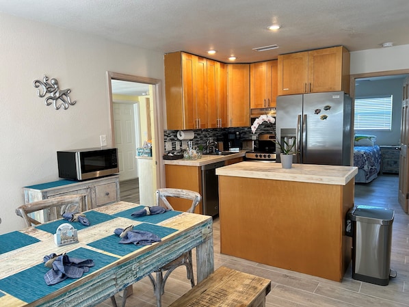 A compact kitchen with wooden cabinets, a stainless steel refrigerator, a microwave, and a dining area with a table and chairs.