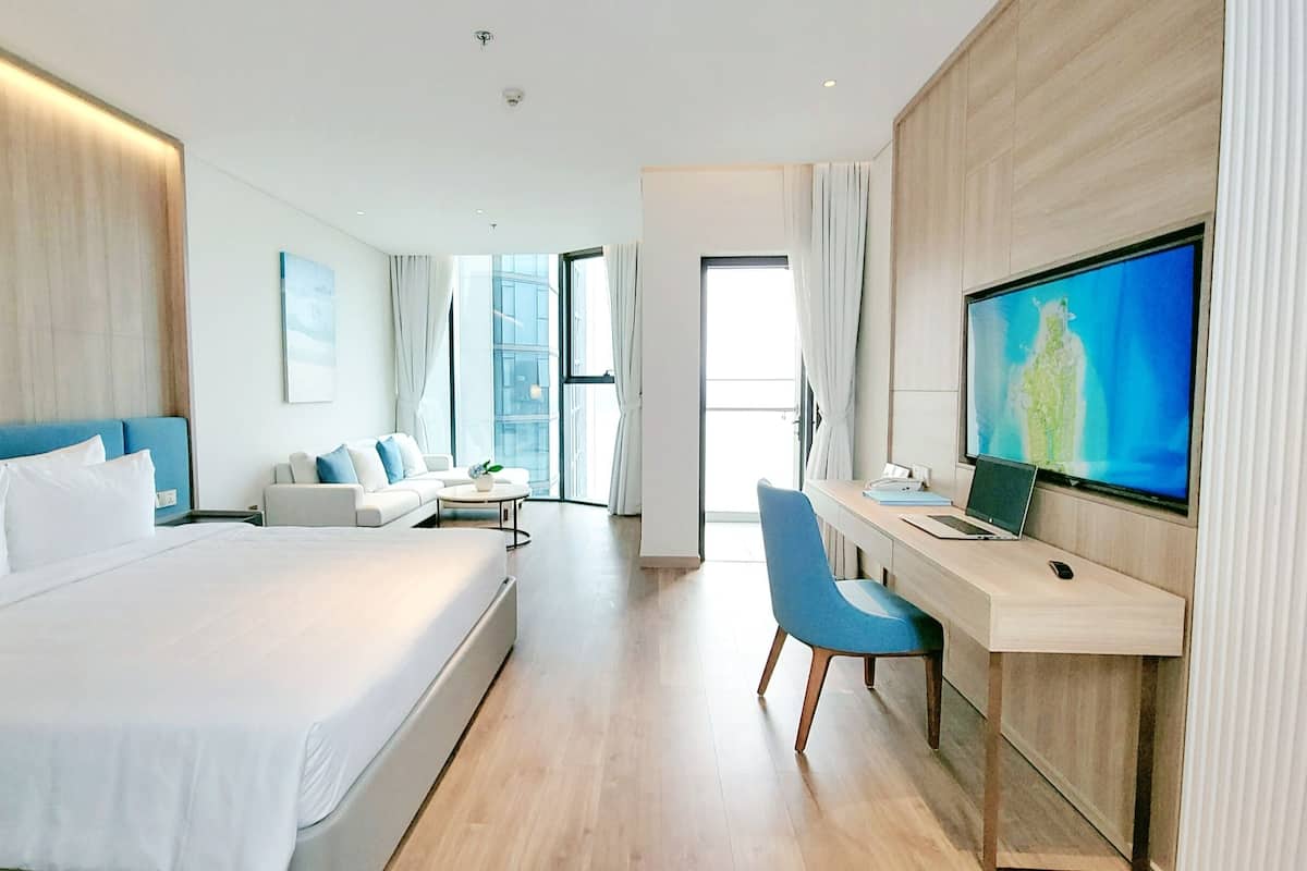 A modern hotel room with a large bed, a desk with a computer, and a TV on the wall.