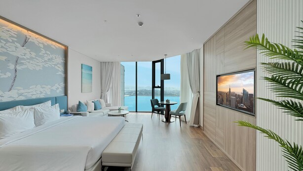 Una habitación de hotel moderna con una cama grande, una zona de estar y vistas a la ciudad.