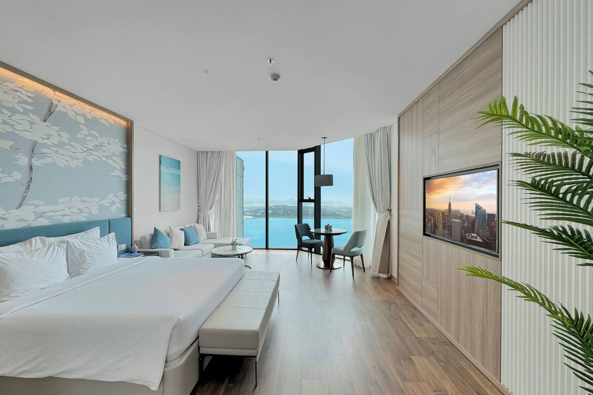 A modern hotel room with a large bed, a seating area, and a view of the city.
