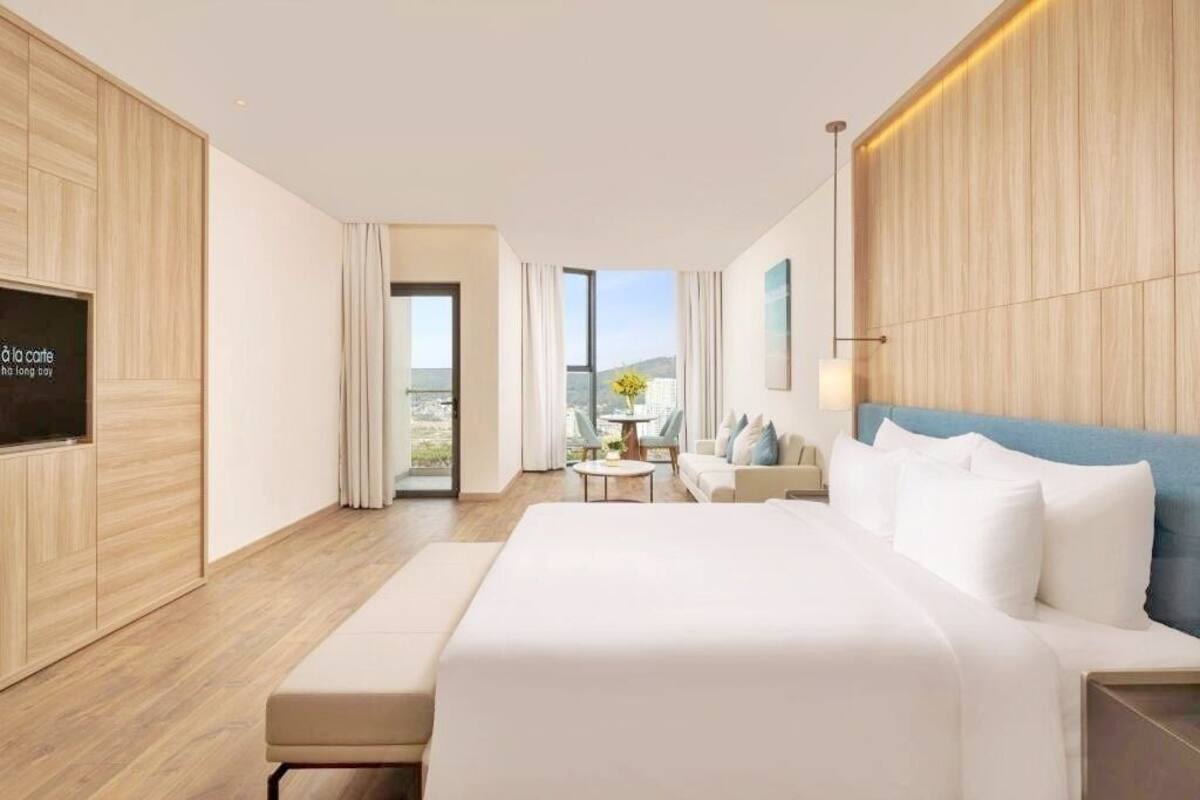 A modern hotel room with a large bed, a seating area, and a view of the city.