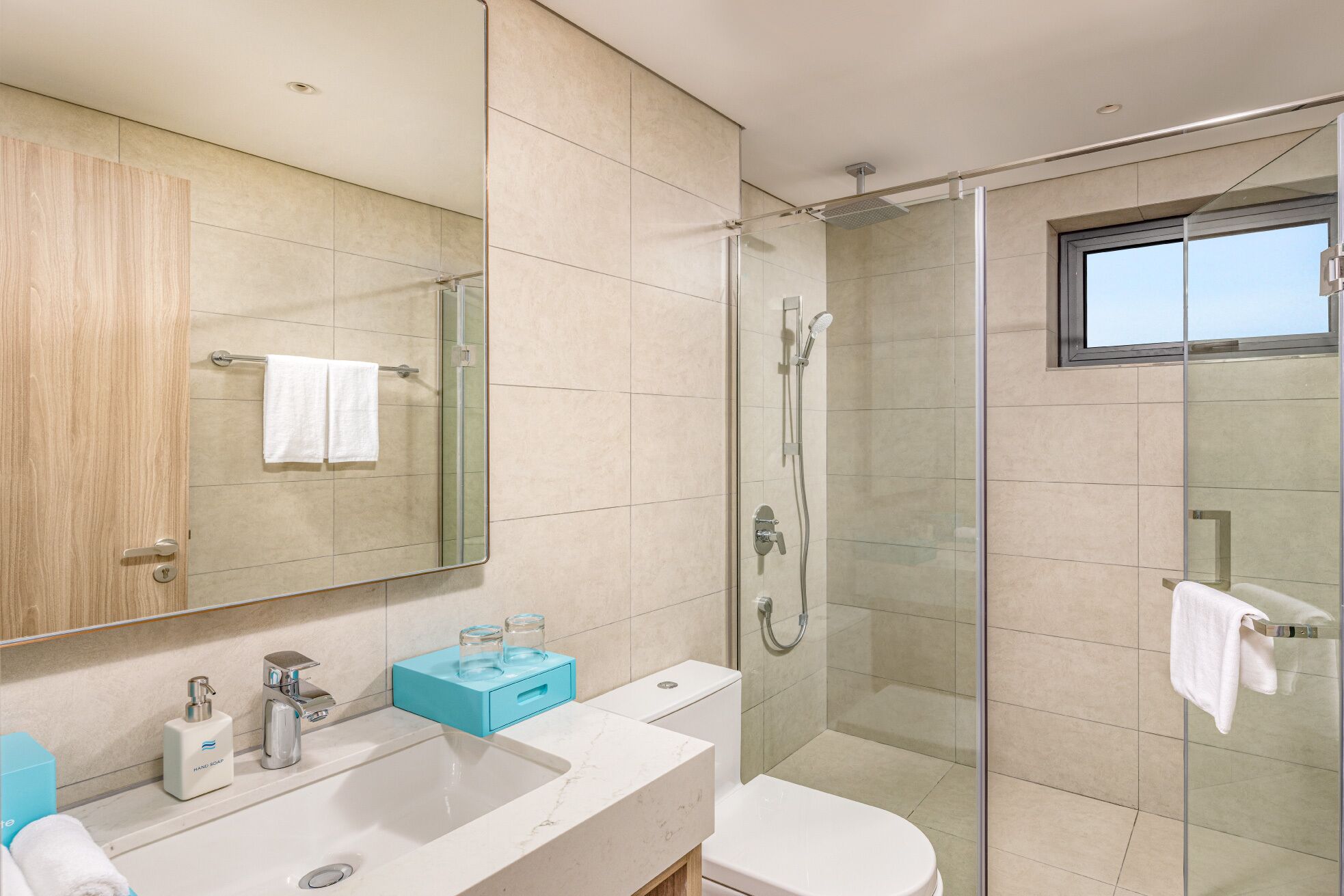Un baño moderno con ducha de vidrio, un espejo grande y un lavabo blanco con dispensador de jabón azul.