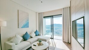 Habitación de hotel moderna con un ventanal grande que ofrece vista a la ciudad, un sofá blanco con cojines azules y una mesa de centro redonda.