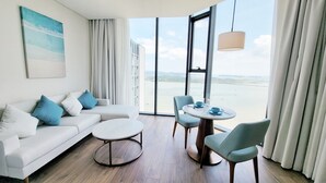 Un moderno cuarto de hotel con un sofá blanco, dos sillas, una mesa redonda y un ventanal con vista al mar.