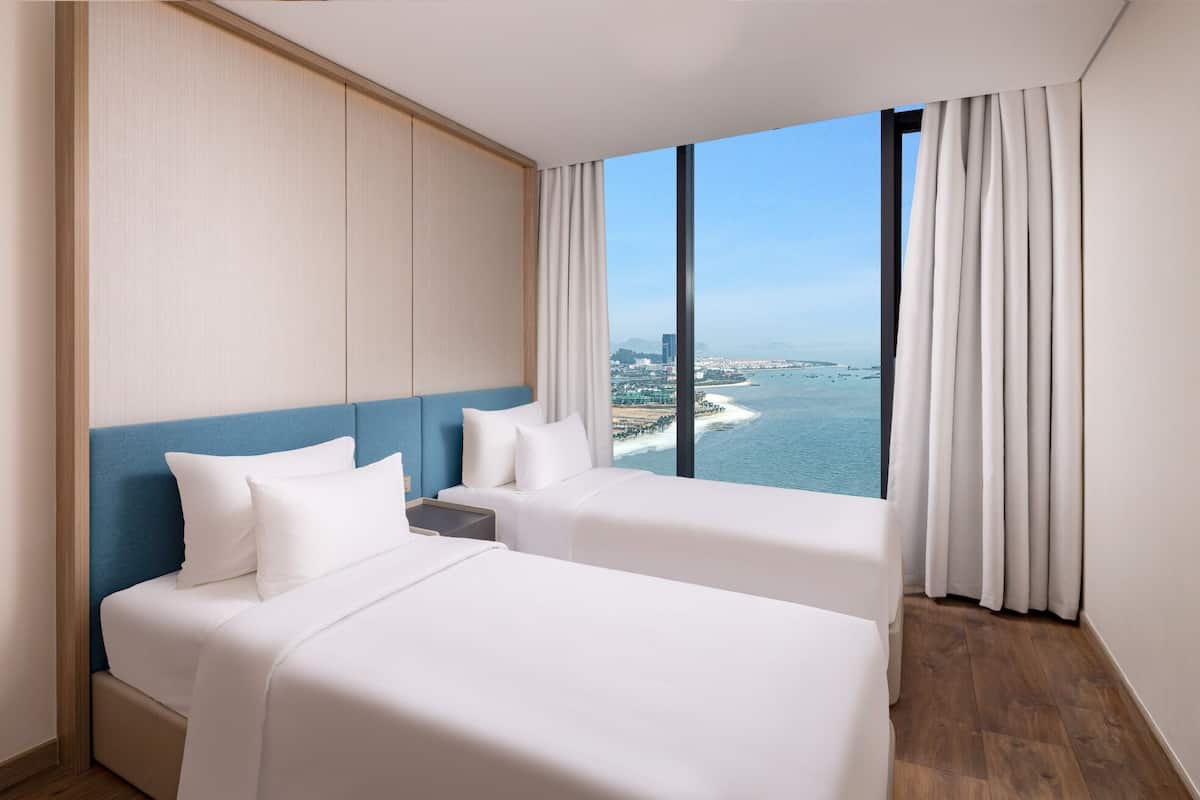 A hotel room with two beds, a view of the sea, and a cityscape.