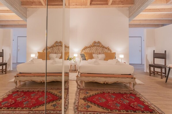 Habitación con espejos, dos camas, cabeceros ornamentados, ropa de cama blanca y alfombras rojas con estampado.