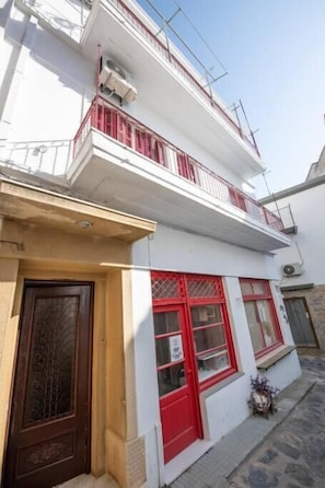 Um edifício de dois andares com fachada branca, janelas emolduradas em vermelho e uma varanda com grades vermelhas.