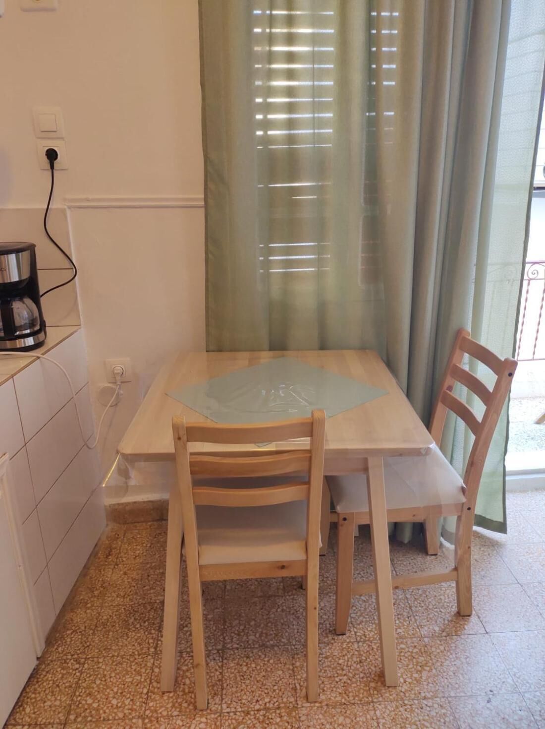 Un petit coin repas avec une table et deux chaises, une machine à café posée sur une étagère et une fenêtre avec des rideaux.