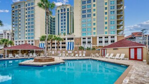 A swimming pool with lounge chairs and a small gazebo, surrounded by tall buildings.