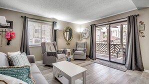 A living room with a sofa, two armchairs, a coffee table, a clock, and a sliding glass door leading to an outdoor balcony.