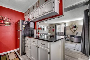A modern kitchen with white cabinets, a black countertop, and a red accent wall. - New! Second Row, First Floor Condo at Waipani-Just 300 Steps to Beach, $300 FREE Activities Daily (North Myrtle Beach)