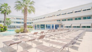 A poolside area with sun loungers, palm trees, and a building with large windows. - Relais du Lac Village - Italian Homing (Desenzano del Garda)
