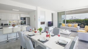 A modern kitchen with white cabinets, a dining area with a white table set for four, and a sofa with yellow cushions.