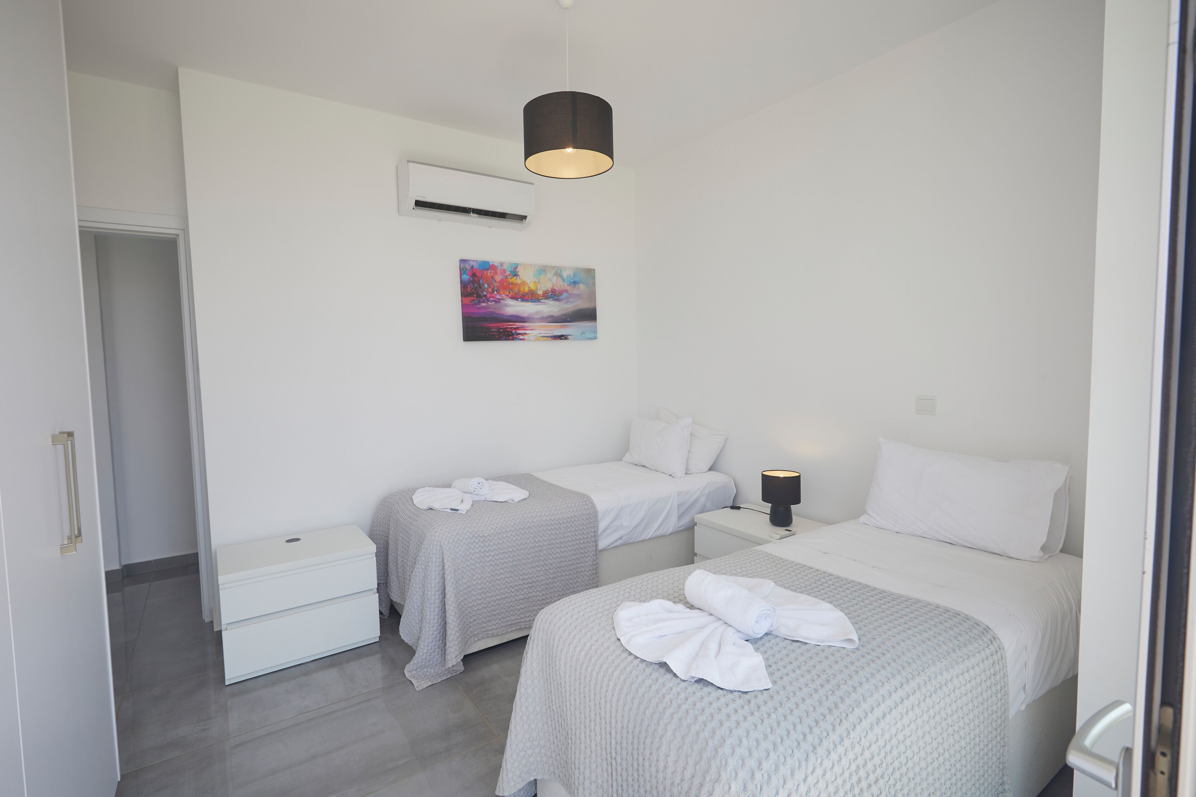 Une chambre d’hôtel avec deux lits, une table de chevet avec une lampe, un climatiseur fixé au mur et un tableau.
