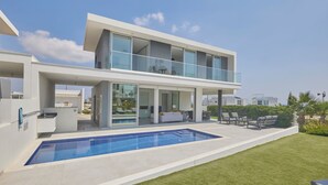 A modern two-story house with a swimming pool, outdoor seating, and a large glass balcony.