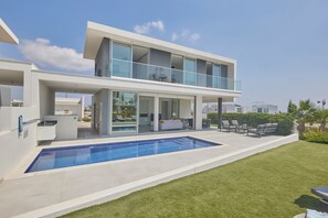 A modern two-story house with a swimming pool, outdoor seating, and a large glass balcony. - Protaras Olivine Villa Ol01 (Paralimni)