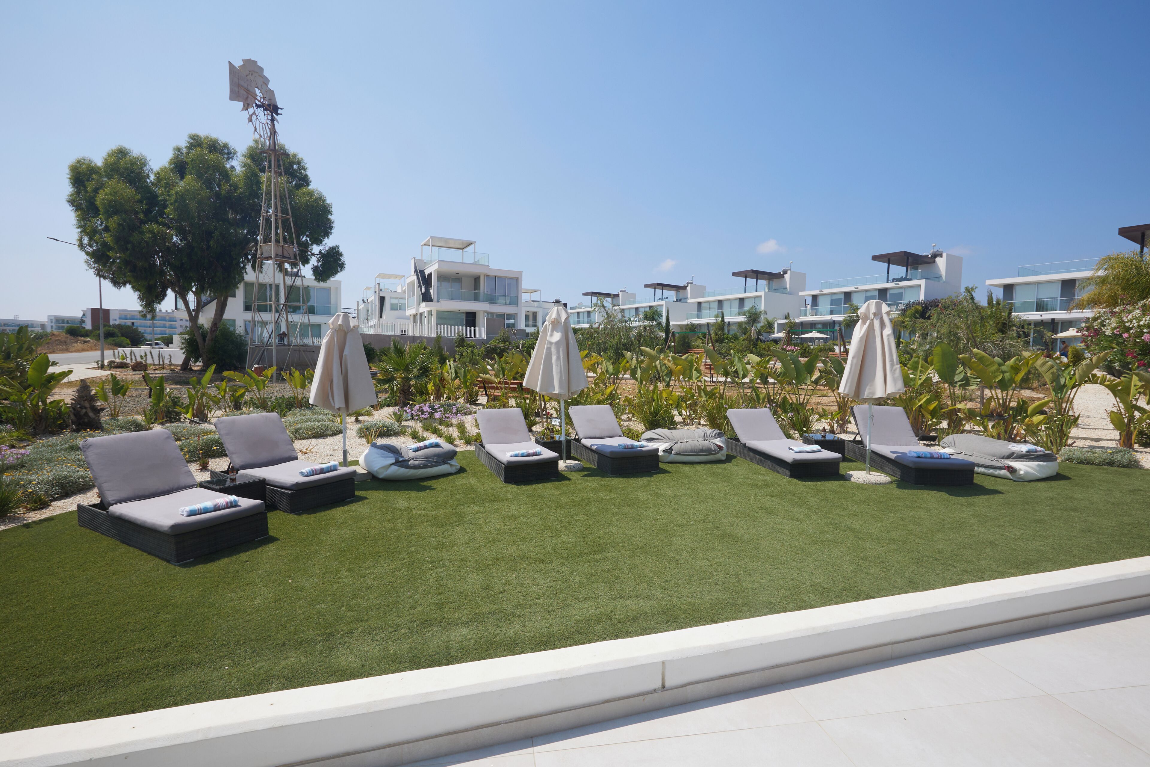 Eine Dachterrasse mit mehreren Liegestühlen und Sonnenschirmen, umgeben von einem gepflegten Rasen und modernen Gebäuden im Hintergrund.