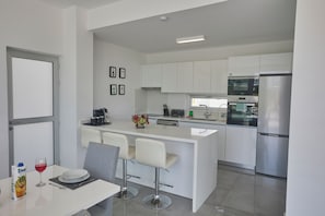 Una cocina moderna con armarios blancos, un refrigerador de acero inoxidable y una barra con dos taburetes.