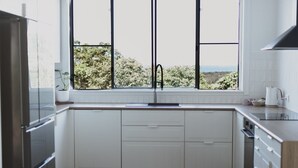 A modern kitchen with white cabinetry, a stainless steel refrigerator, a double sink, and a window with a view of greenery. - Victoria St. Beach House, Coffs Jetty
5 Bedroom PET Friendly Airconditioned (Coffs Harbour)