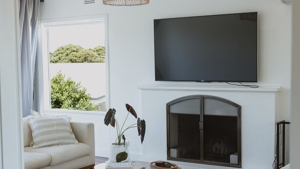 A living room with a sofa, a fireplace, a television, and a window with a view of greenery. - Victoria St. Beach House, Coffs Jetty
5 Bedroom PET Friendly Airconditioned (Coffs Harbour)