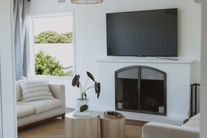 A living room with a sofa, a fireplace, a television, and a window with a view of greenery. - Victoria St. Beach House, Coffs Jetty
5 Bedroom PET FRIENDLY Airconditioned (Coffs Harbour)
