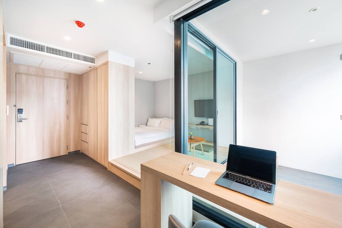 A modern room with a bed, a desk with a laptop, and a sliding door.