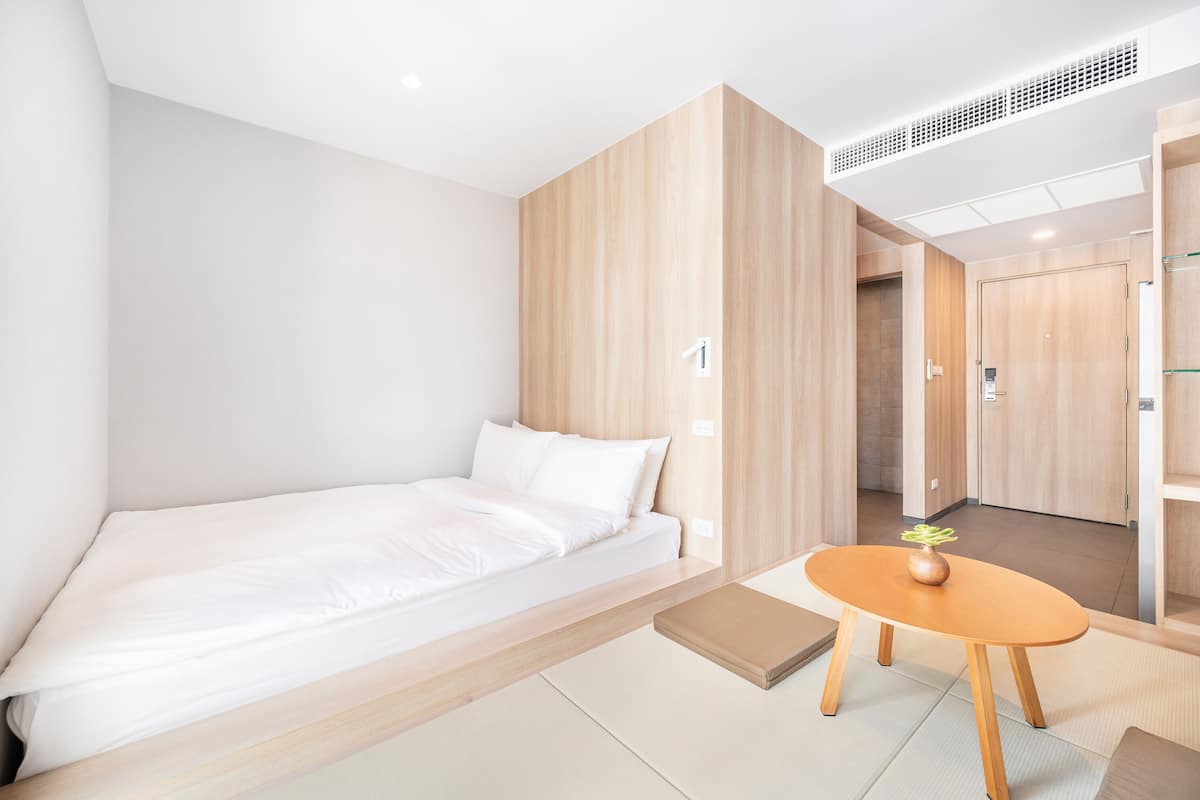 A minimalist hotel room with a single bed, a small wooden table, and a walk-in closet.