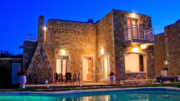 Un edificio de piedra con piscina, mobiliario exterior y balcón.