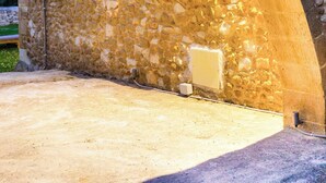 Un edificio de piedra con una ventana bajo un arco, un enchufe eléctrico visible y un suelo de hormigón.