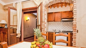 A room with a dining table set with fruit, wooden cabinets, and a kitchen area with a stove. - Stunning Views of the Baia de Bahas Residence 1 Bedroom Premium Sleeps 4 (Golfo Aranci)