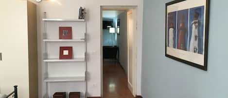 A hallway with a white shelving unit, a framed picture of lighthouses, and a wooden floor.