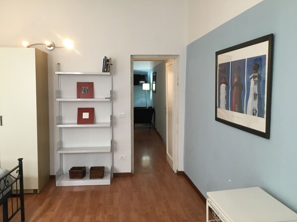 A hallway with a white shelving unit, a framed picture of lighthouses, and a wooden floor.