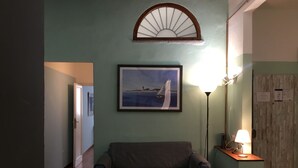 A room with a sofa, a framed painting of a sailboat, a wall-mounted fan, and a lamp. - Servi 39 in Firenze With 2 Bedrooms and 2 Bathrooms (Florence)
