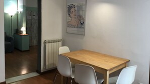 A dining area with a wooden table and white chairs, a radiator, a framed picture on the wall, and a lamp in the background. - Servi 39 in Firenze With 2 Bedrooms and 2 Bathrooms (Florence)