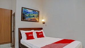 A neatly made bed with white bedding and red accents, a wooden headboard, and a wall-mounted painting above it. - Hotel O Jr Residence Syariah (Medan)