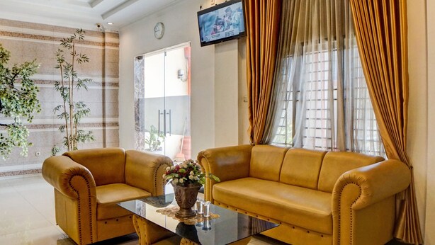 A living room with two yellow sofas, a glass coffee table, and a TV mounted on the wall. - Hotel O Jr Residence Syariah (Medan)