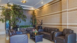 A lobby with leather sofas, a coffee table, and a large potted plant. - Hotel O Jr Residence Syariah (Medan)