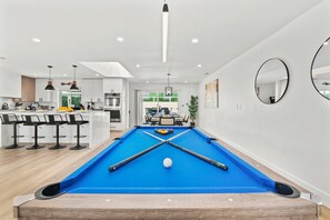 Une cuisine moderne équipée d’une table de billard, de tabourets de bar et d’un coin repas offrant une vue sur l’extérieur.