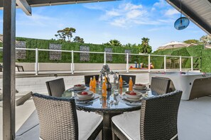 Une terrasse extérieure avec une table ronde dressée pour le repas, entourée de chaises en osier, et un jacuzzi en arrière-plan.