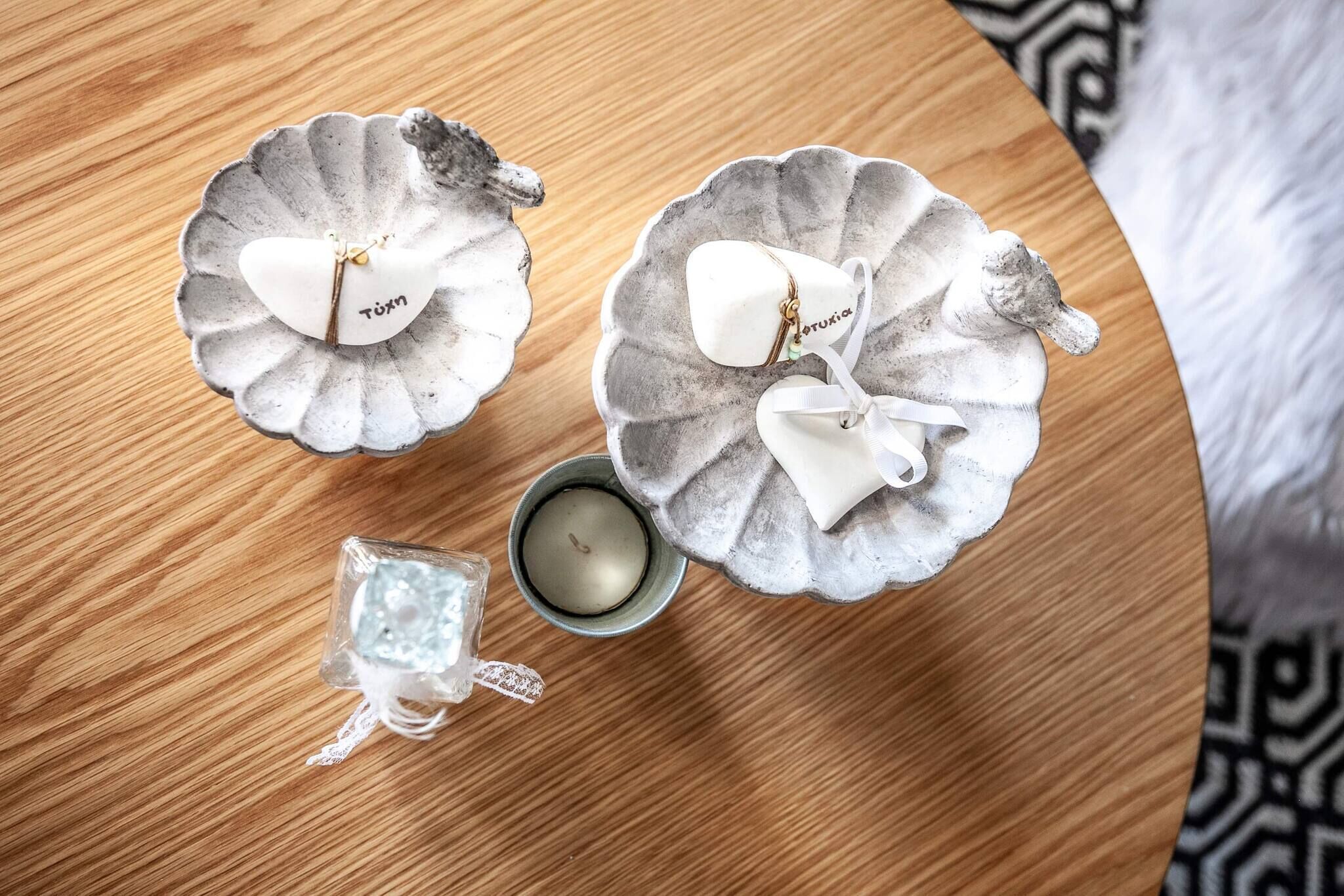 Dos recipientes de cerámica con forma de corazón con nombres encima de una mesa de madera, una vela pequeña y un tarro de cristal con un lazo.