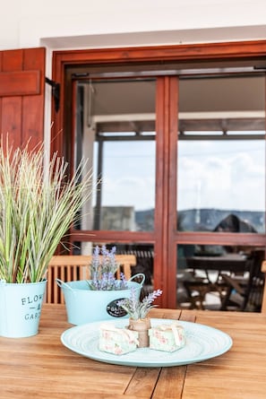 A wooden table with a plate of food, potted plants, and a view of a building through a window. - Vila Vasiliki, Next To Platanias, 6min From Sea! (Platanias)