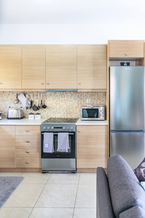 Compact kitchen with modern appliances and a cozy seating area featuring a sofa and patterned cushion.