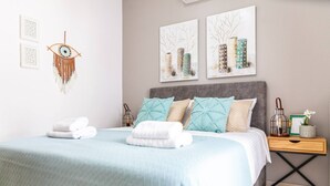 Ein ordentlich bezogenes Bett mit blauer Bettdecke, ein Nachttisch mit Lampe und Wandbild.