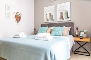A neatly made bed with a blue bedspread, a bedside table with a lamp, and wall art. - Vila Vasiliki, Next To Platanias, 6min From Sea! (Platanias)