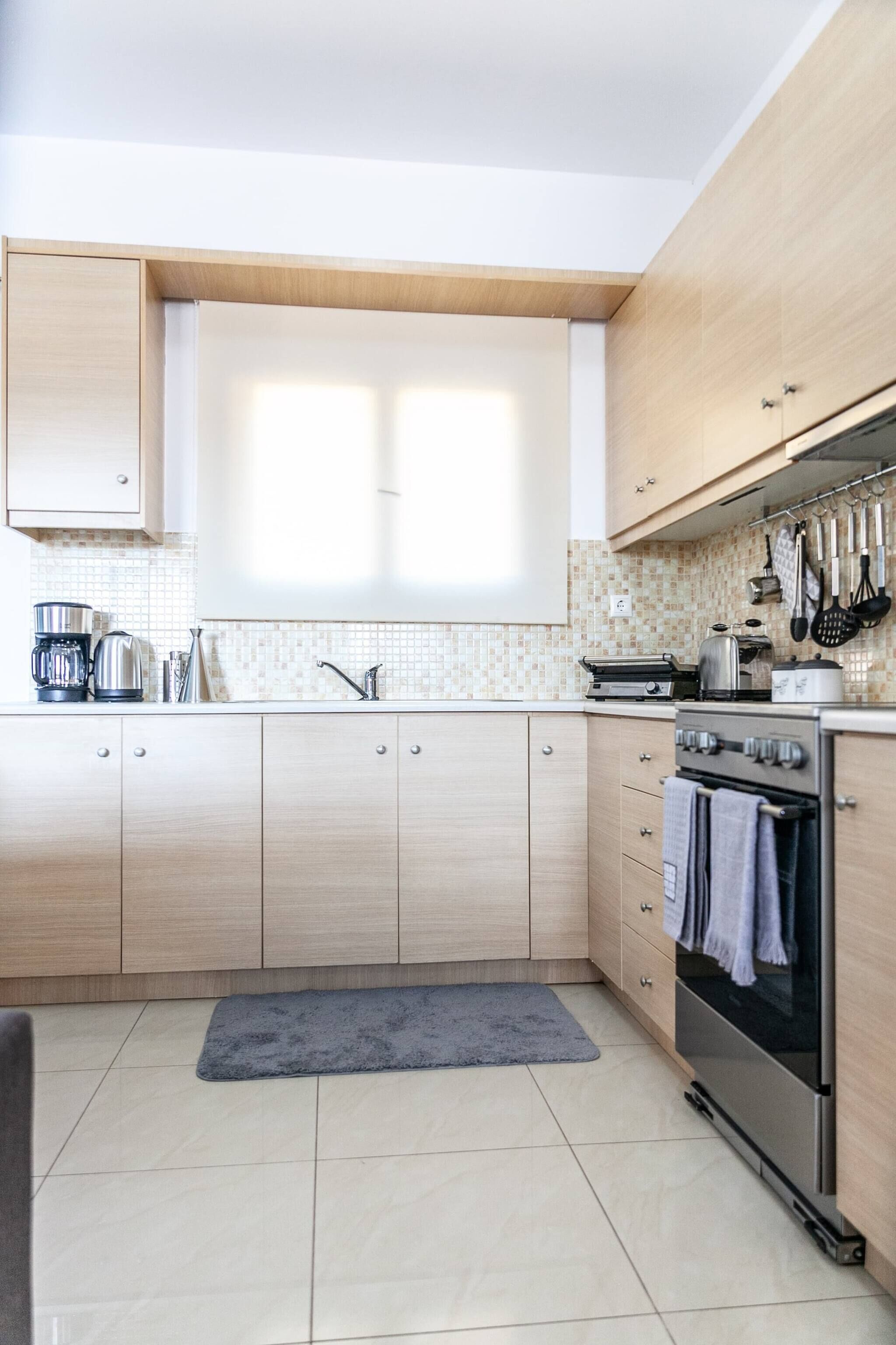 A modern kitchen with light wood cabinets, a stainless steel oven, a coffee maker, and a tiled backsplash.