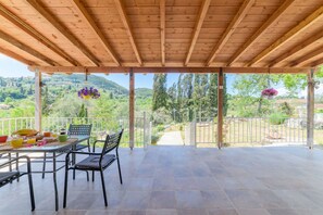 Eine überdachte Terrasse mit Frühstückstisch, Stühlen und hängenden Blumenkörben.